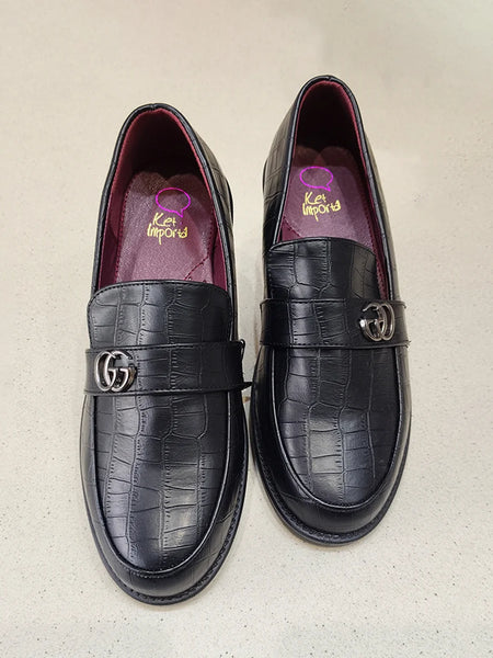 Pair of black crocodile-textured loafers with Gucci logo on a beige background