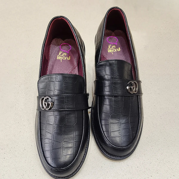 Pair of black crocodile-textured loafers with Gucci logo on a beige background