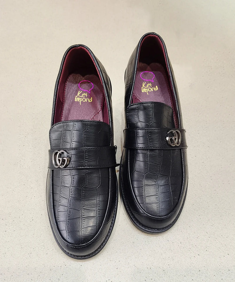 Pair of black crocodile-textured loafers with Gucci logo on a beige background