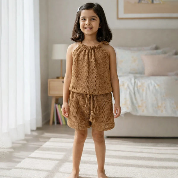 Young girl wearing a brown knitted outfit standing in a bedroom.