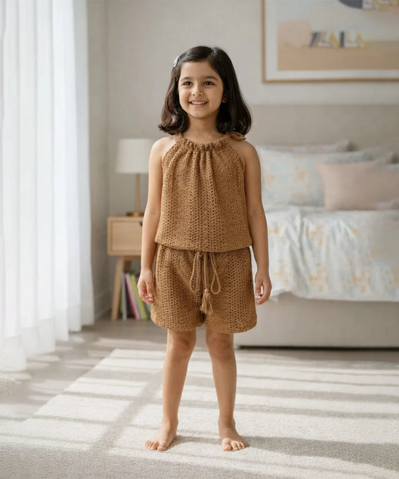 Young girl wearing a brown knitted outfit standing in a bedroom.