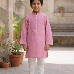 Young boy wearing a pink kurta with white pants standing outdoors.