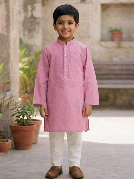 Young boy wearing a pink kurta with white pants standing outdoors.