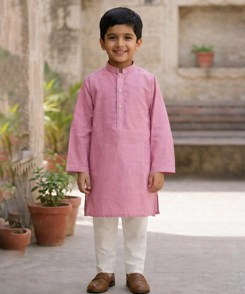 Young boy wearing a pink kurta with white pants standing outdoors.