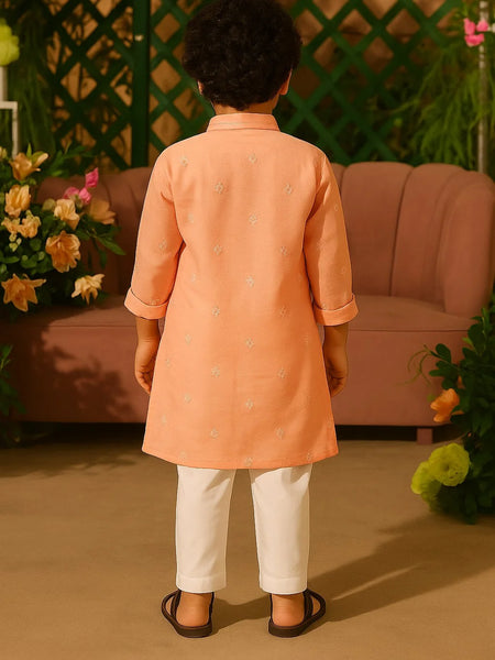 Child wearing an orange kurta with white pants standing in a decorated room.