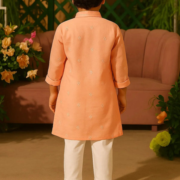 Child wearing an orange kurta with white pants standing in a decorated room.
