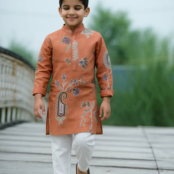 Child wearing an embroidered orange kurta with white pants on a wooden deck.