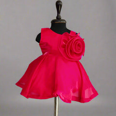 Fuchsia pink dress with large rose embellishment on mannequin against plain background.