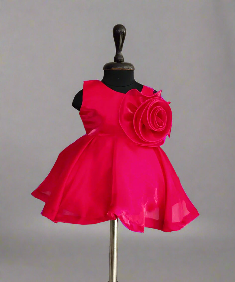 Fuchsia pink dress with large rose embellishment on mannequin against plain background.