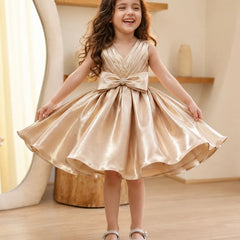 Young girl in a gold dress with a large bow standing indoors.