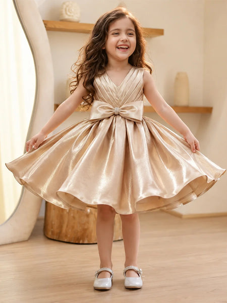 Young girl in a gold dress with a large bow standing indoors.
