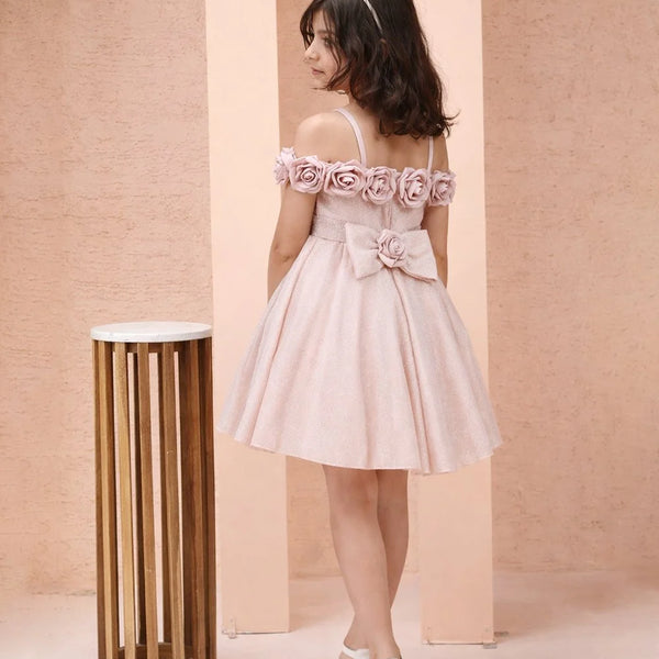 Young girl in a pink floral dress standing against a beige wall with a small round table.