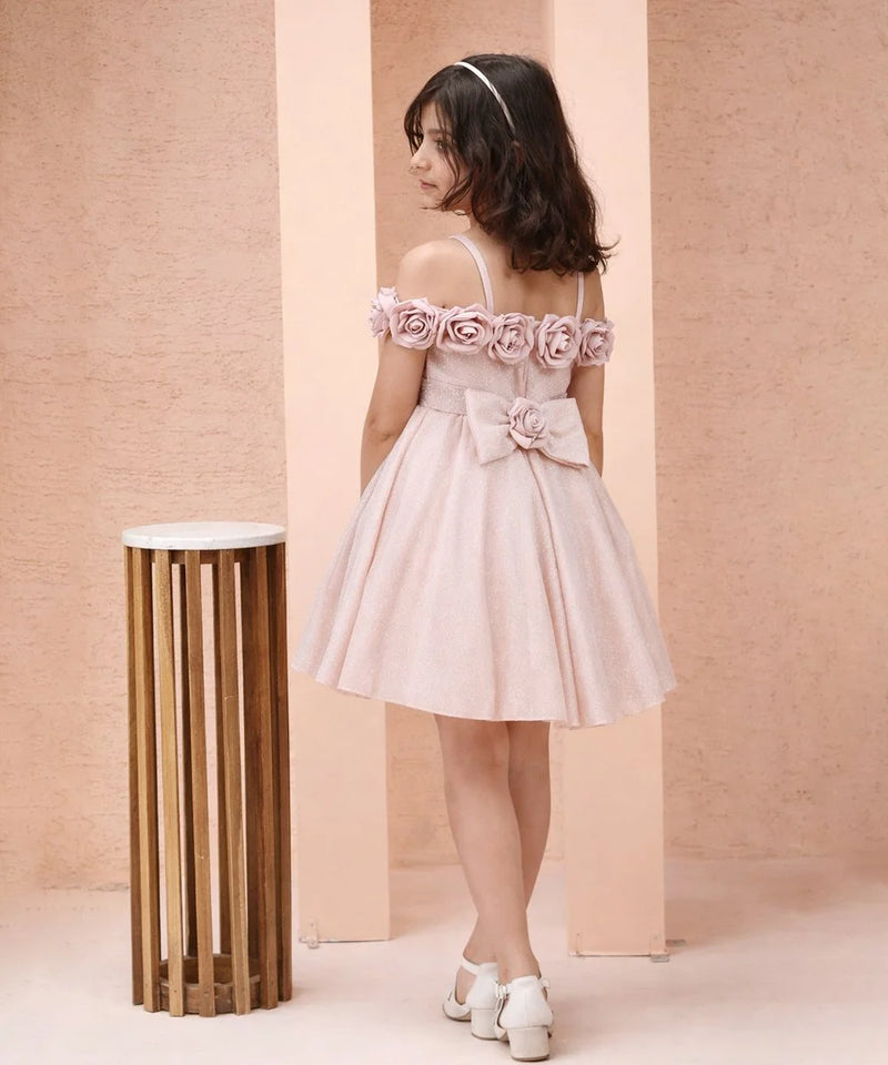 Young girl in a pink floral dress standing against a beige wall with a small round table.