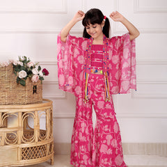 Child wearing a pink floral outfit with arms raised in a room with a wicker table and flowers.