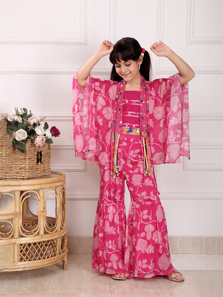 Child wearing a pink floral outfit with arms raised in a room with a wicker table and flowers.