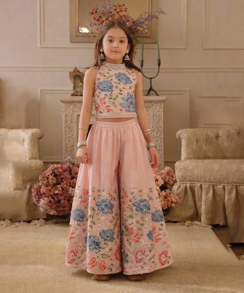 Young girl in a floral top and pink pants standing in an elegant room.