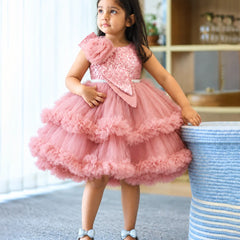 A young girl wearing a pink sequined and tulle party dress, standing next to a blue-and-white striped basket in an indoor room.