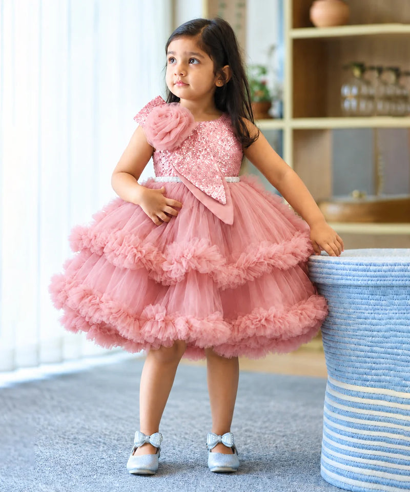 A young girl wearing a pink sequined and tulle party dress, standing next to a blue-and-white striped basket in an indoor room.