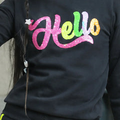 A close-up of a person wearing a black long-sleeve top with a colorful glittery 'Hello' graphic across the chest in pink, green, yellow, and orange.
