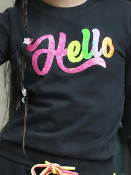 A close-up of a person wearing a black long-sleeve top with a colorful glittery 'Hello' graphic across the chest in pink, green, yellow, and orange.