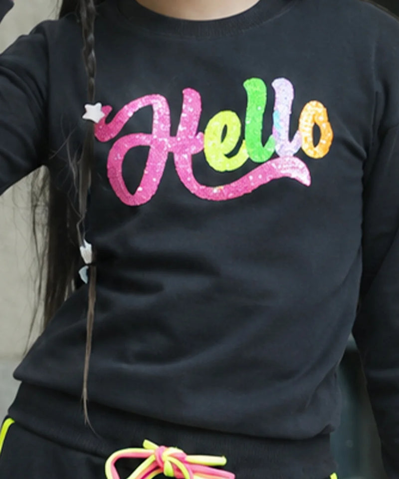 A close-up of a person wearing a black long-sleeve top with a colorful glittery 'Hello' graphic across the chest in pink, green, yellow, and orange.