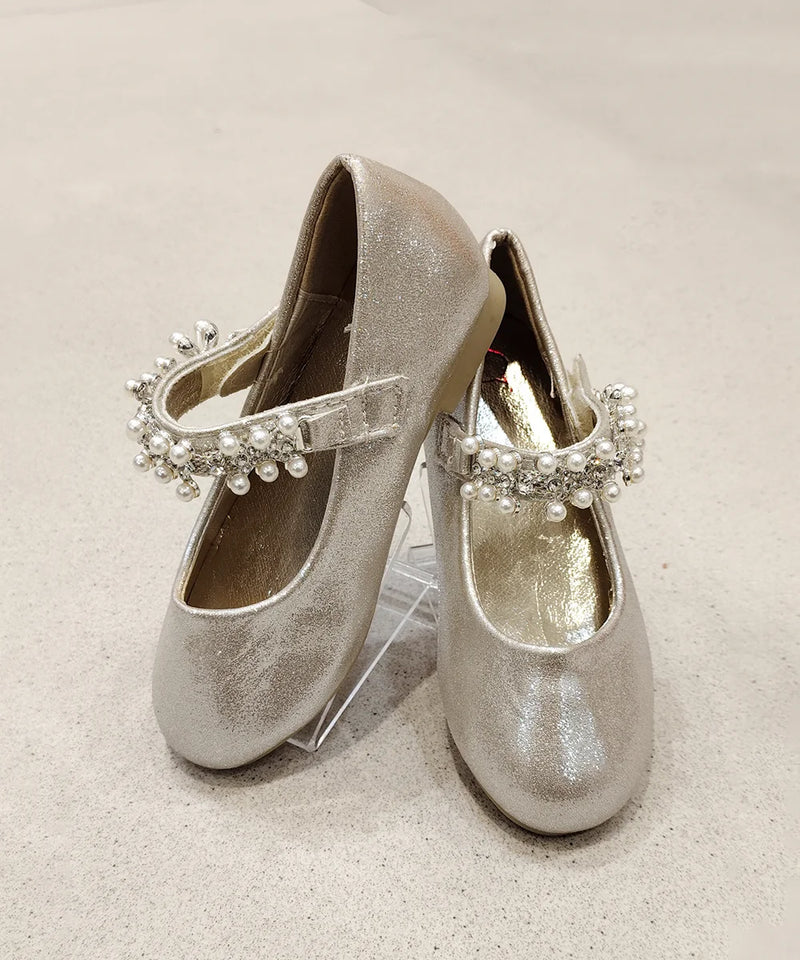 Pair of silver glittery shoes with decorative straps on a light background