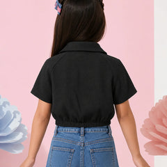 A child model shown from the back wearing a black short-sleeve collared shirt and blue jeans, standing against a pink background with decorative paper flowers.