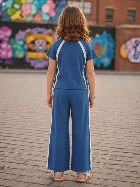 Person wearing a blue outfit with white stripes standing on a brick pavement in front of colorful murals.