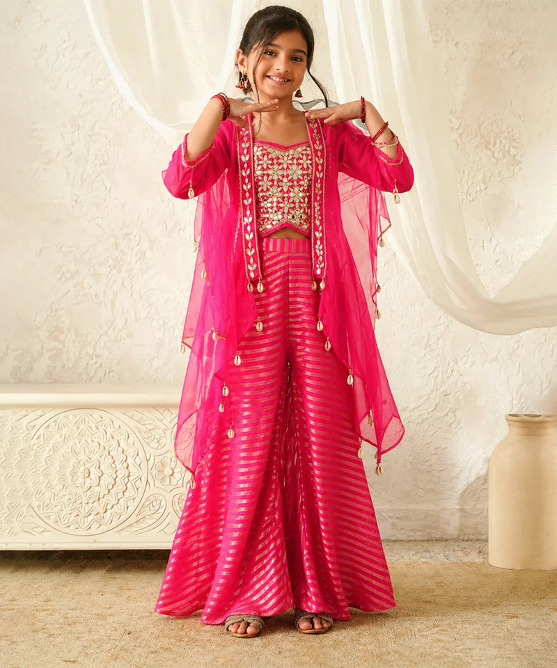 Woman in a pink traditional outfit with gold accents against a white curtain background
