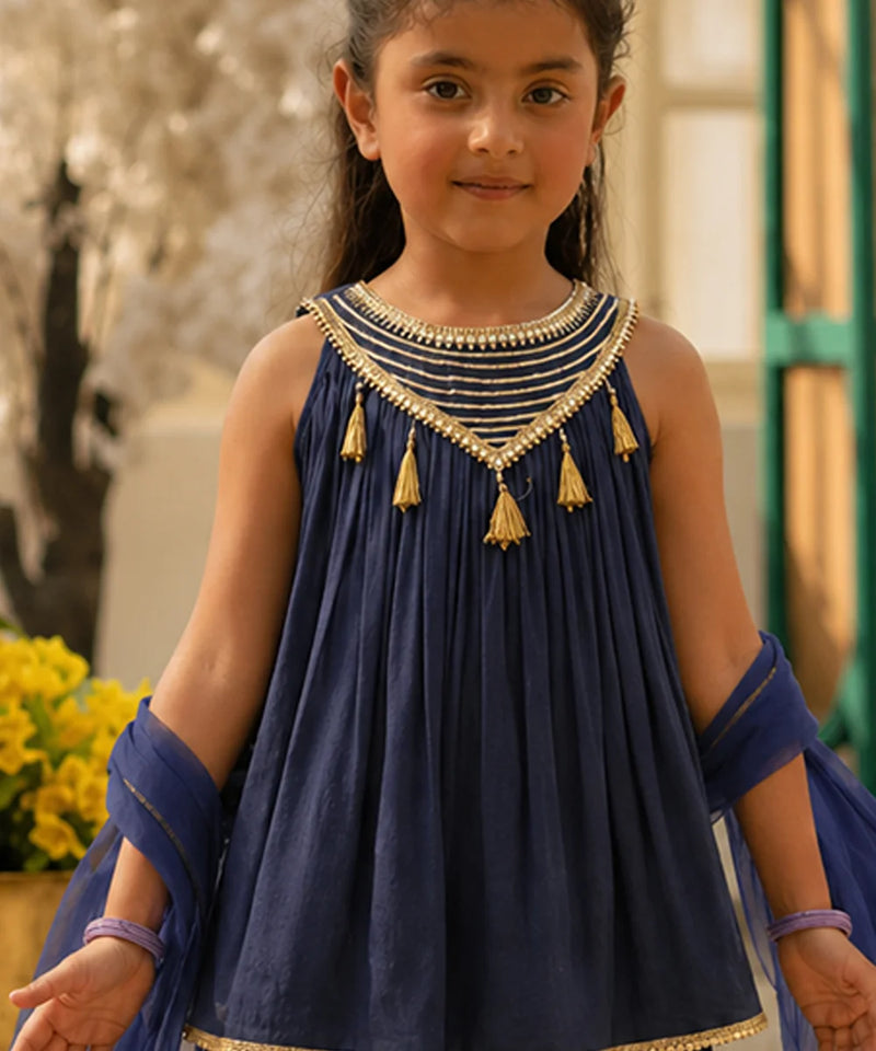 Young girl wearing a blue traditional outfit with gold details outdoors.