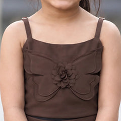 A child model shown from behind wearing a brown two-piece outfit consisting of a smocked camisole top and matching wide-leg trousers, standing in an outdoor plaza.