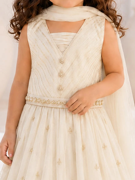A child wearing a sleeveless cream or ivory formal dress with a V-neck bodice, decorative front buttons, a beaded waistband, and a flowing skirt with small embroidered motifs. A matching sheer scarf is draped over the shoulders.