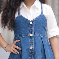 A child wearing a blue denim camisole-style vest with front buttons over a white collared shirt, shown from the shoulders to the hips against a softly blurred outdoor background.