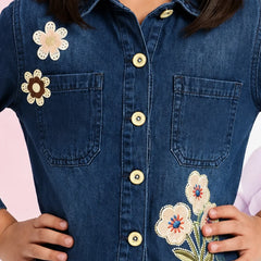 A close-up of a person wearing a dark blue denim button-up shirt with embroidered flowers on the chest and pocket.