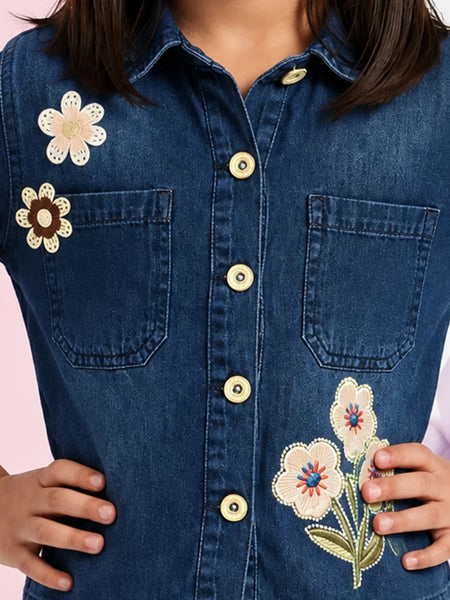 A close-up of a person wearing a dark blue denim button-up shirt with embroidered flowers on the chest and pocket.