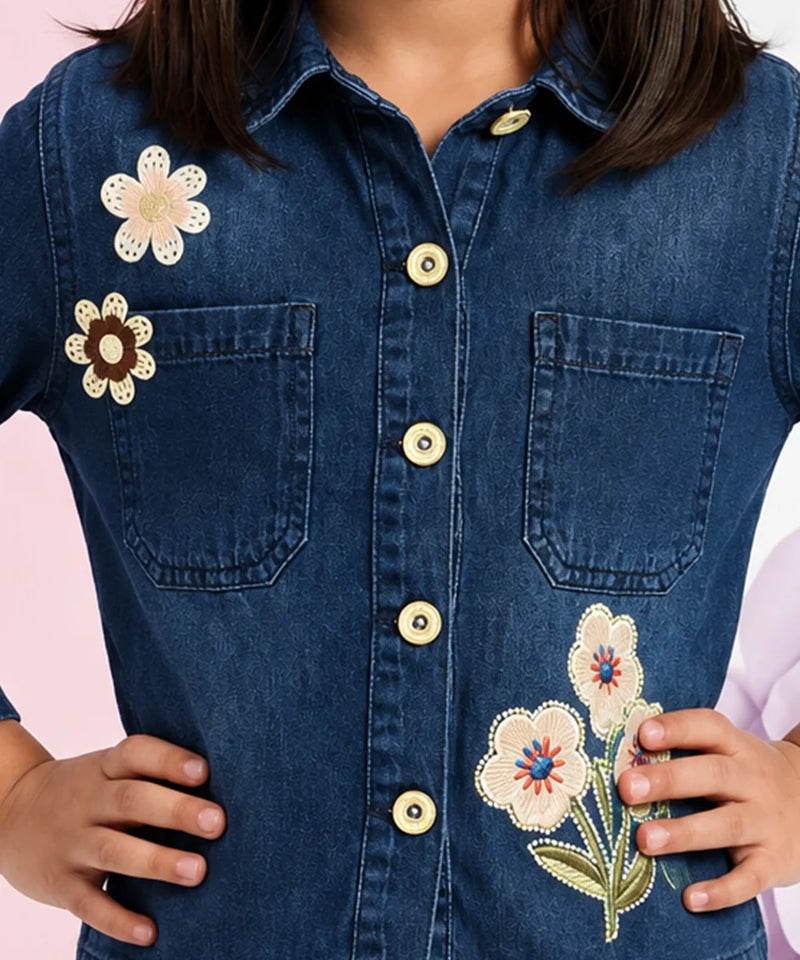 A close-up of a person wearing a dark blue denim button-up shirt with embroidered flowers on the chest and pocket.