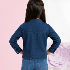 A child model shown from the back wearing a dark blue denim jacket and matching blue jeans, standing against a split pink and white background with a decorative purple flower on the right.