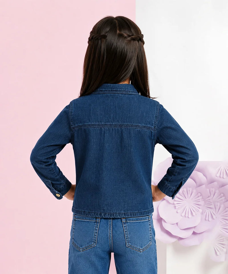 A child model shown from the back wearing a dark blue denim jacket and matching blue jeans, standing against a split pink and white background with a decorative purple flower on the right.
