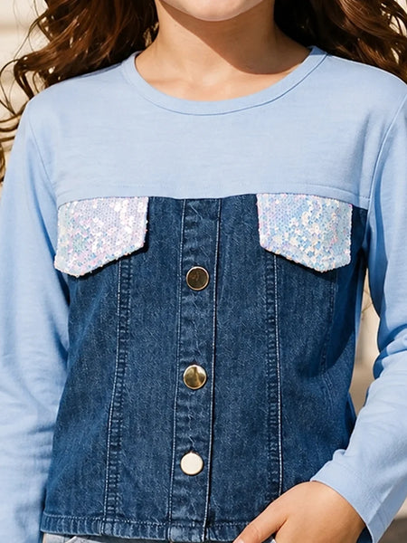 A close-up of a child wearing a light blue long-sleeve top with a dark blue denim-style front panel, sequined flap pockets, and gold-tone buttons.