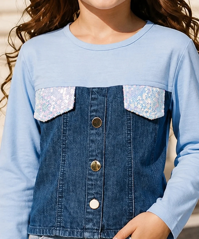 A close-up of a child wearing a light blue long-sleeve top with a dark blue denim-style front panel, sequined flap pockets, and gold-tone buttons.