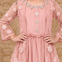 A pink traditional Indian dress with intricate floral embroidery and beadwork, shown on a model against a patterned beige background.