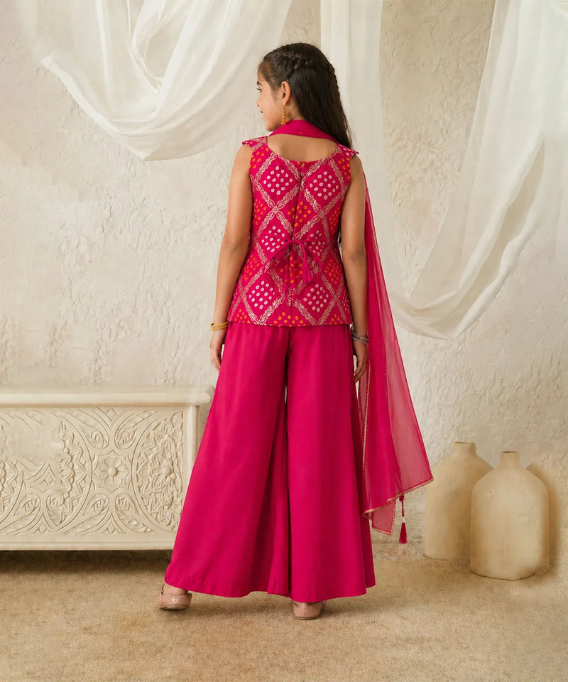 Woman in a pink traditional outfit standing in a room with white curtains and decorative elements.