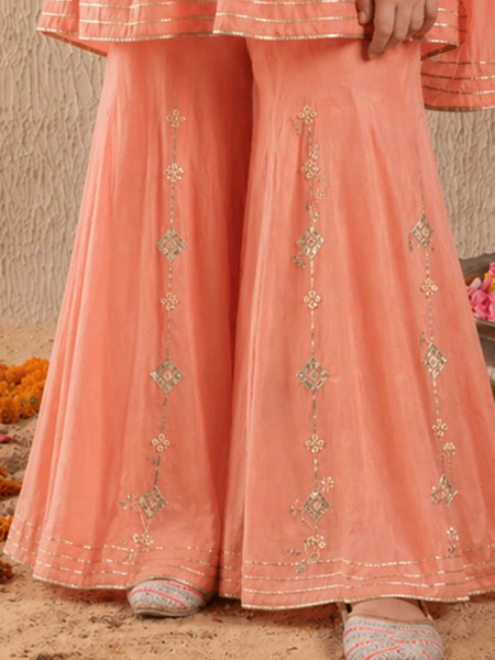 Peach-colored traditional outfit with intricate patterns on a sandy background
