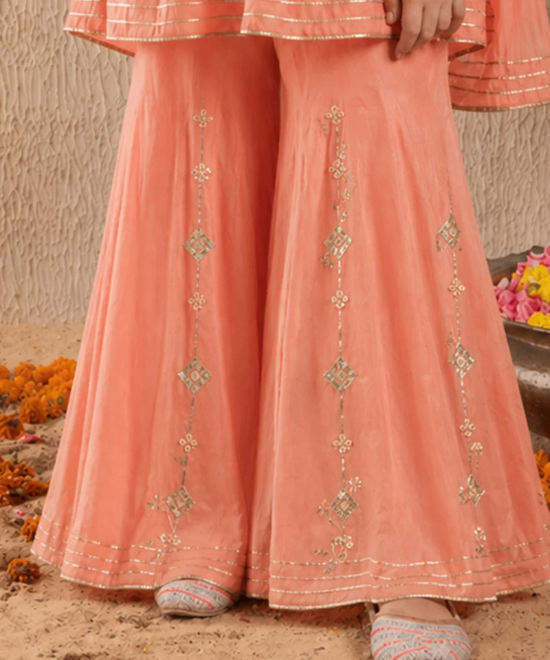 Peach-colored traditional outfit with intricate patterns on a sandy background