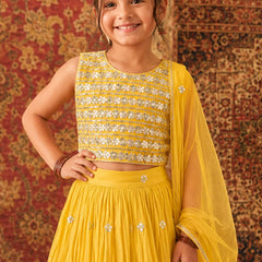 Young girl in a yellow traditional outfit with sequins against a patterned wall.
