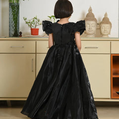 Child wearing a black dress with puffed sleeves in a room with light-colored cabinets and decorative items.