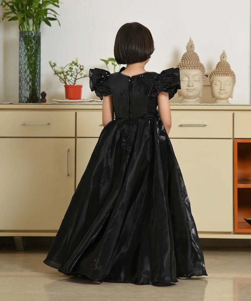 Child wearing a black dress with puffed sleeves in a room with light-colored cabinets and decorative items.