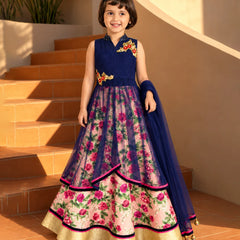 A young girl stands on terracotta steps wearing a sleeveless navy blue and floral pink traditional dress with gold embroidery and a matching navy dupatta.