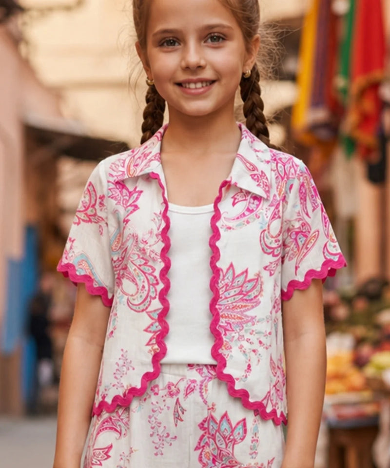 Young girl wearing a pink and white patterned outfit with a blurred outdoor background