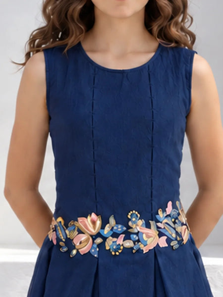 A sleeveless navy blue dress with vertical pleats and a colorful floral embroidered waistband, shown on a model against a light gray background.